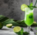Grüner Cocktail vor grauem Hintergrund mit Limetten