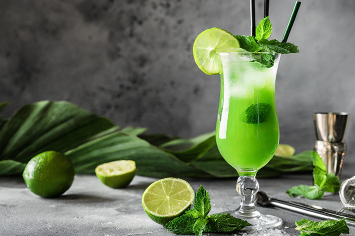 Grüner Cocktail vor grauem Hintergrund mit Limetten